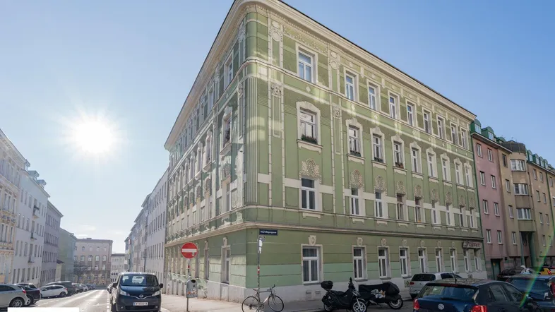 Elegantes Eckgebäude mit klassischer grüner Fassade und Stuckverzierungen an einem sonnigen Tag in der Stadt.