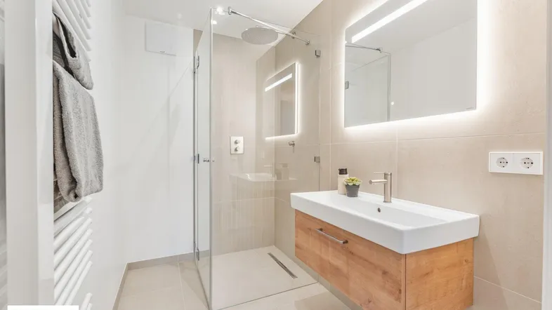 Modernes Badezimmer mit begehbarer Dusche, schwebendem Waschtisch und beleuchtetem Spiegel.