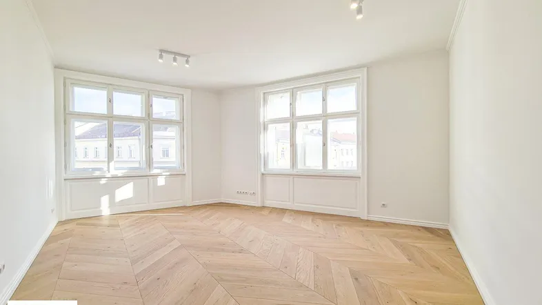 Helles, leeres Zimmer mit Fischgrätparkett und großen Fenstern, bereit zur individuellen Gestaltung.