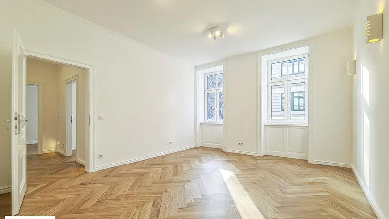 Helles, leeres Zimmer mit Fischgrätparkettboden und zwei großen Fenstern, bereit zur Einrichtung.