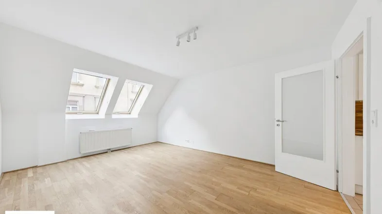 Helles Dachgeschosszimmer mit schrägen Wänden, Dachfenstern und Parkettboden, ideal als Wohnraum.