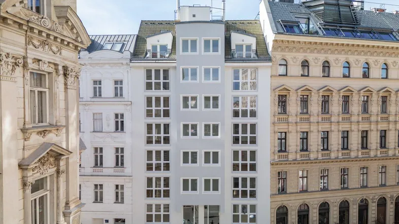 Modernes Wohngebäude mit vielen Fenstern, umgeben von historischen Altbauten in der Stadt.