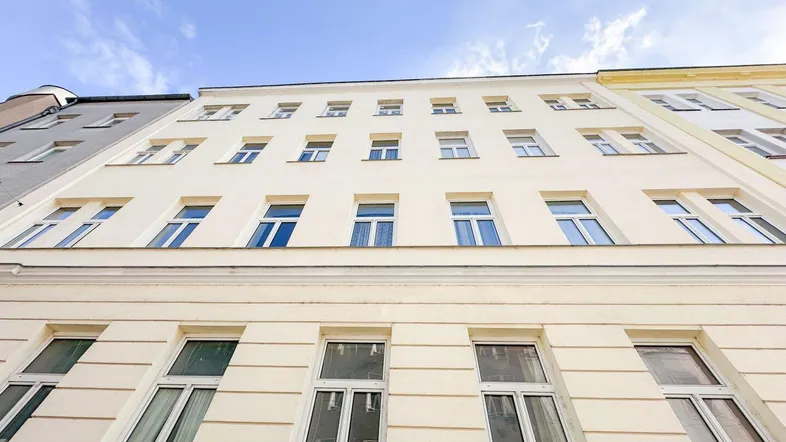 Klassische Gebäudefassade mit vielen Fenstern und einer hellen Putzfassade unter blauem Himmel.