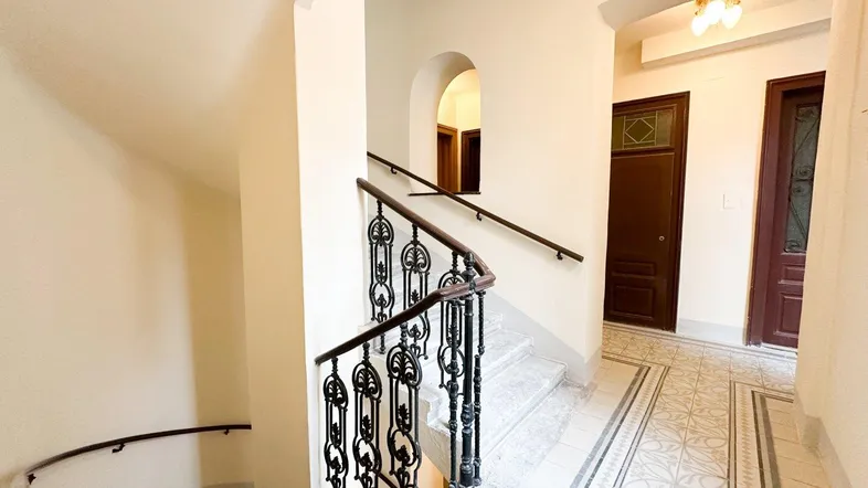Historisches Treppenhaus mit kunstvollem schmiedeeisernem Geländer und gemusterten Fliesenböden.