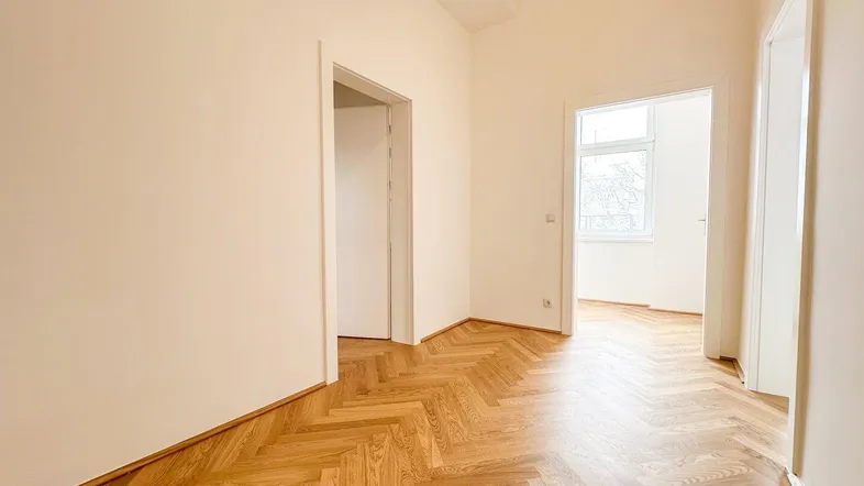 Helles Zimmer mit Fischgrätparkett und weißen Wänden, bereit zur individuellen Gestaltung.