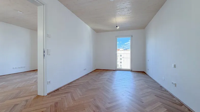 Helles, leeres Zimmer mit Fischgrätparkett und Zugang zu einem französischen Balkon.
