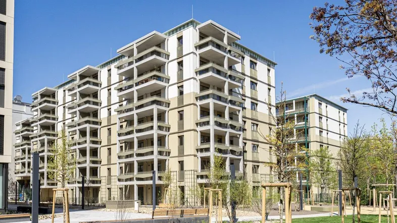 Moderne Wohngebäude mit zahlreichen Balkonen und begrünten Außenanlagen unter blauem Himmel.