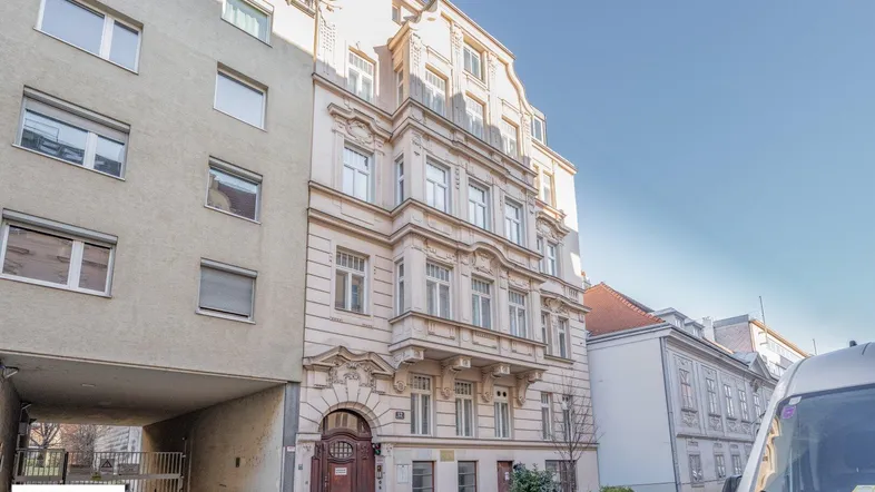 Fassade eines Altbaus mit angrenzendem modernen Gebäude und einer Einfahrt zum Innenhof.
