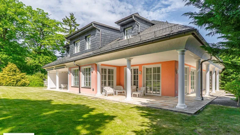 Elegante Villa mit weitläufigem Garten und überdachter Terrasse, umgeben von viel Grün.