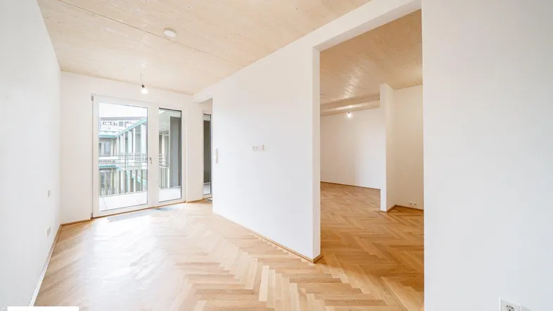 Helles Zimmer mit Fischgrätparkettboden und Zugang zu einem Balkon, ideal für einen Wohnbereich.