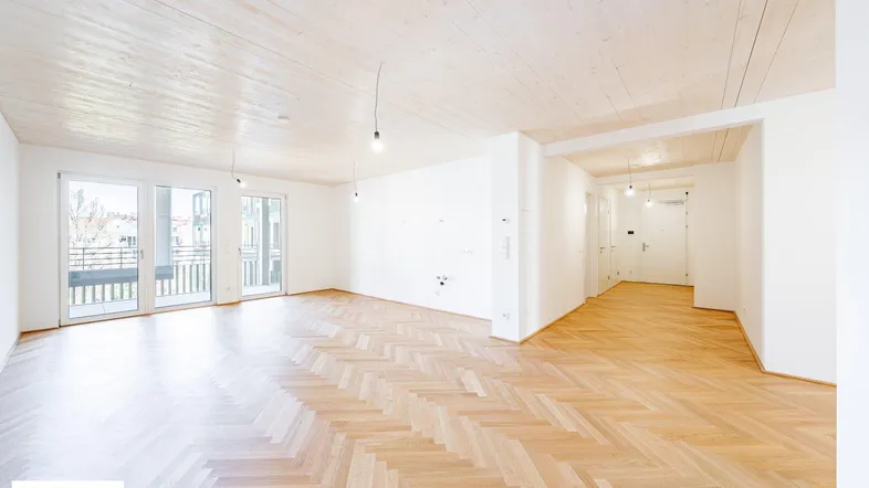 Helles, geräumiges Wohnzimmer mit elegantem Fischgrätparkett, Holzbalkendecke und Zugang zum Balkon.