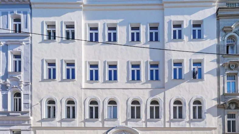 Die weiße Fassade eines klassisch renovierten Wohngebäudes mit vielen Fenstern.
