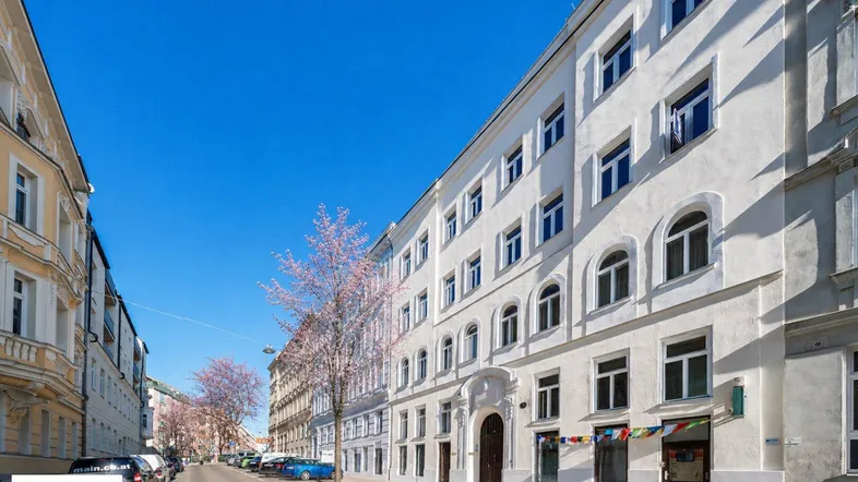 Historisches Gebäude mit weißer Fassade und vielen Fenstern an einer belebten Straße.