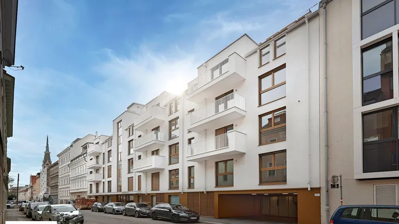 Moderne Wohngebäude-Fassade mit weißen Balkonen und großen Fenstern an einer sonnigen Stadtstraße.