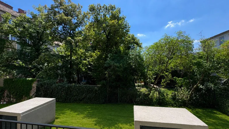 Grüner Gartenbereich mit Rasenfläche und Bäumen, gesehen von einem Balkon oder einer Terrasse.