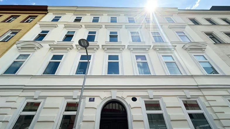 Klassische Fassade eines Mehrfamilienhauses mit vielen Fenstern und Sonnenschein.