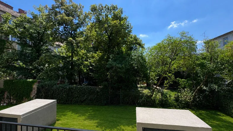 Blick auf eine gepflegte grüne Rasenfläche mit Bäumen und blauem Himmel, umgeben von Gebäuden.
