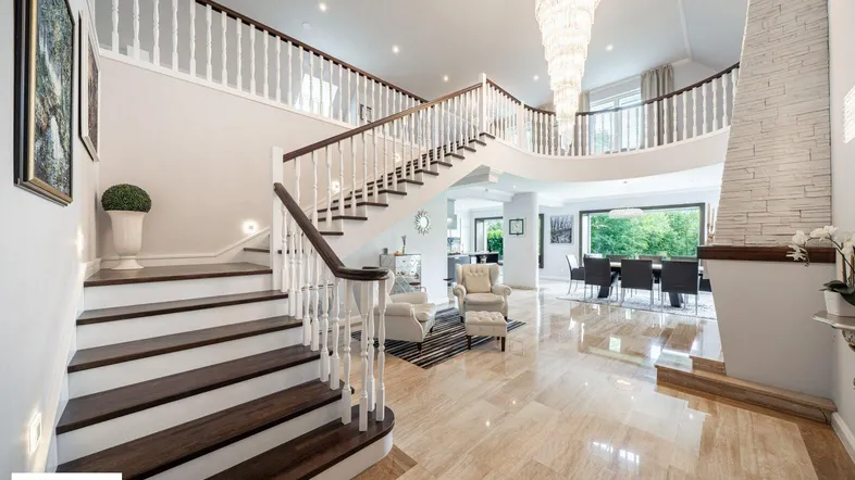 Großzügige Eingangshalle mit eleganter Treppe, Marmorboden und Kronleuchter, die zu weiteren Wohnbereichen führt.
