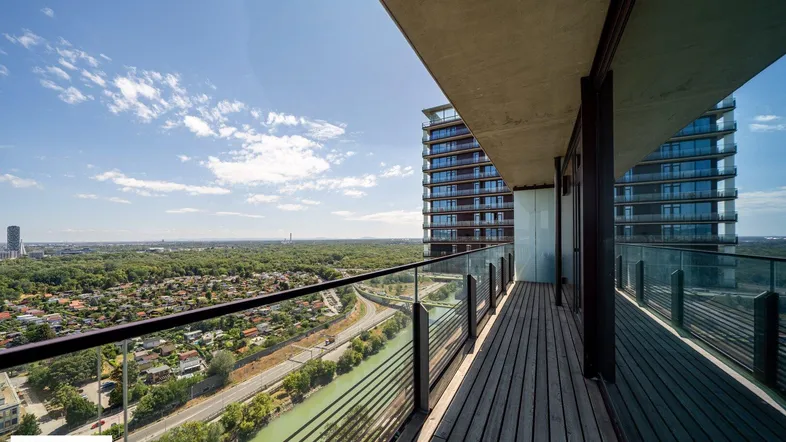 Geräumiger Balkon mit Holzboden und Glasgeländer bietet einen weiten Blick über die Stadt und den Fluss.