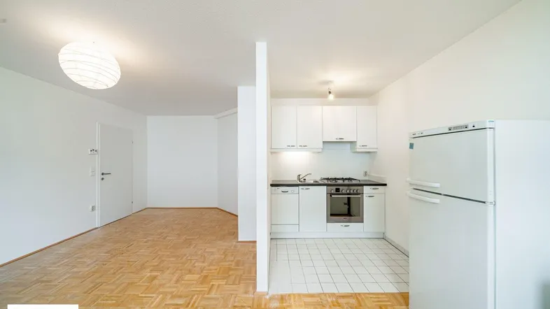 Heller Wohnbereich mit Parkettboden und integrierter Küchenzeile in einem modernen Apartment.