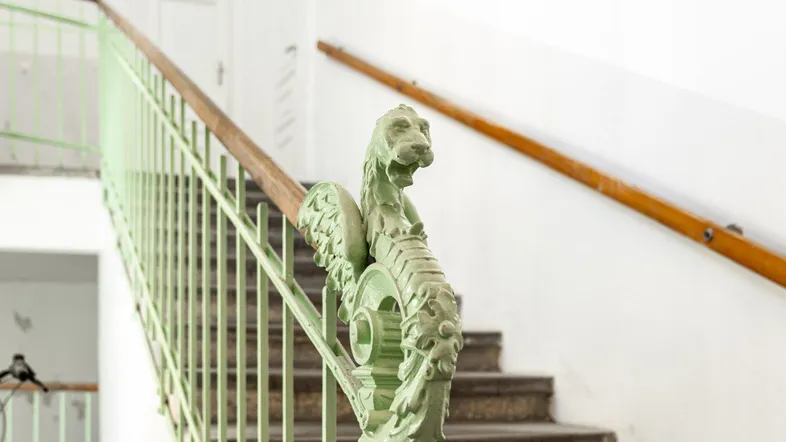 Detailansicht eines historischen Treppenhauses mit kunstvollem grünen Geländer und Holzhandlauf.