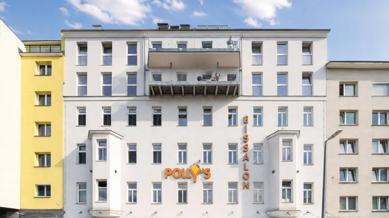 Moderne Fassade eines Mehrfamilienhauses mit Geschäften im Erdgeschoss und einem kleinen Balkon.