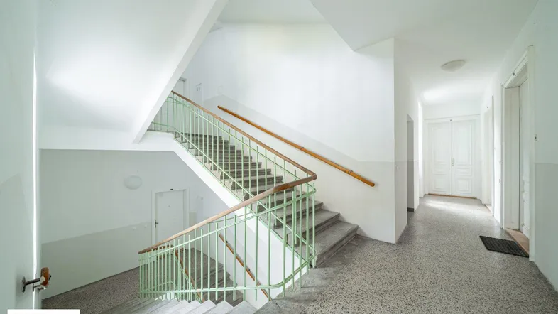 Helles Treppenhaus mit Terrazzoboden und grünem Geländer in einem Mehrfamilienhaus.