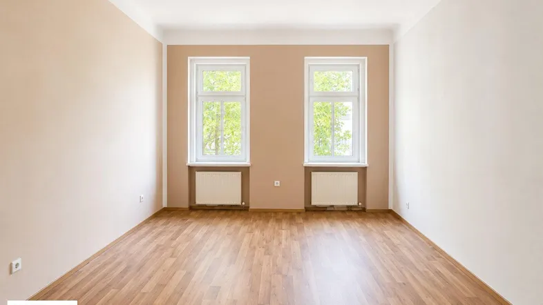 Helles, leeres Zimmer mit Parkettboden und zwei Fenstern, bereit zur individuellen Gestaltung.