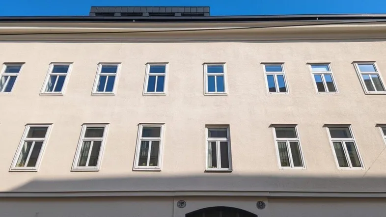Historische Fassade eines Mehrfamilienhauses mit zahlreichen Fenstern unter blauem Himmel.