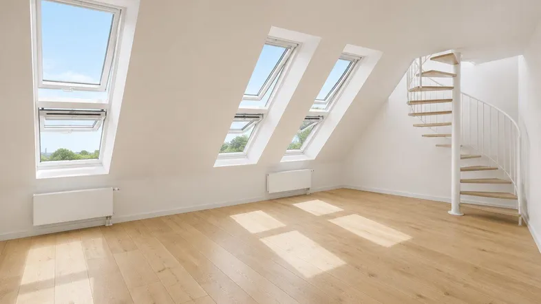 Heller Dachbodenraum mit Holzfußboden, mehreren Dachfenstern und einer eleganten Wendeltreppe.