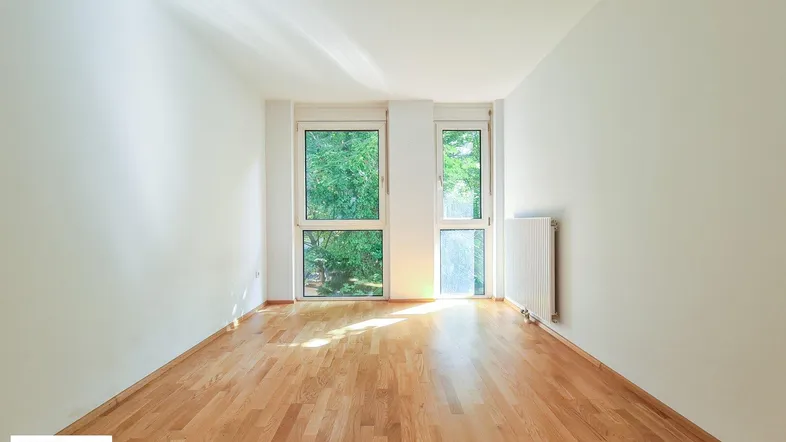 Helles Zimmer mit großen Fenstern, Parkettboden und Blick ins Grüne.
