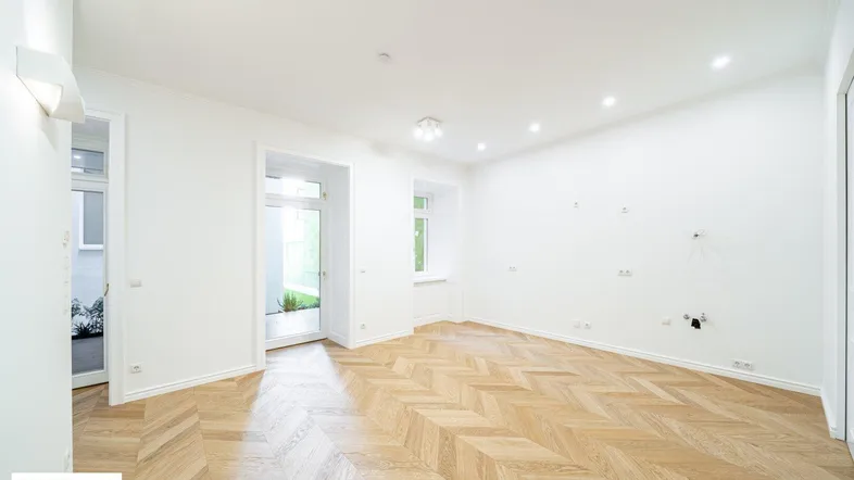 Helles Zimmer mit Fischgrätparkett und Zugang zu einem Außenbereich, ideal als Wohnzimmer nutzbar.