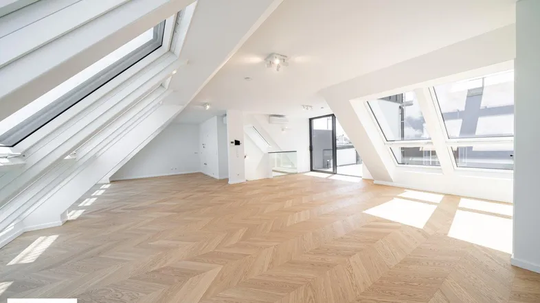 Helles, offenes Dachgeschosszimmer mit Fischgrätparkett, großen Dachfenstern und Zugang zur Terrasse.