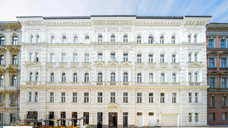 Weißes, historisches Gebäude mit reich verzierter Fassade und vielen Fenstern unter blauem Himmel.