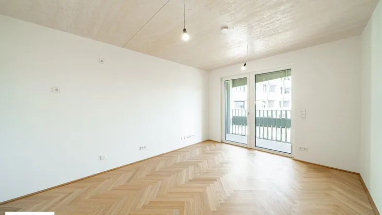 Helles Zimmer mit Fischgrätparkett, Holzbalkendecke und Zugang zu einem Balkon.