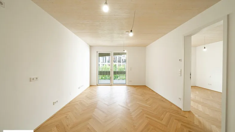 Heller Raum mit Fischgrätparkett, Holzbalkendecke und Zugang zu einem Balkon, ideal für Wohn- oder Schlafbereich.