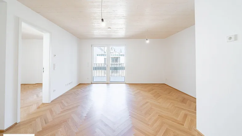 Helles, leeres Wohnzimmer mit Fischgrätparkettboden, Holzdecke und Zugang zu einem Balkon.