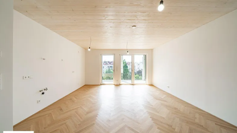 Heller, leerer Raum mit Fischgrätparkett, Holzdecke und Zugang zu einem Balkon.