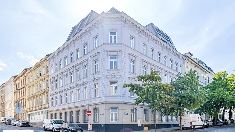 Historisches Eckgebäude in städtischer Umgebung mit klassischer Architektur und vielen Fenstern.