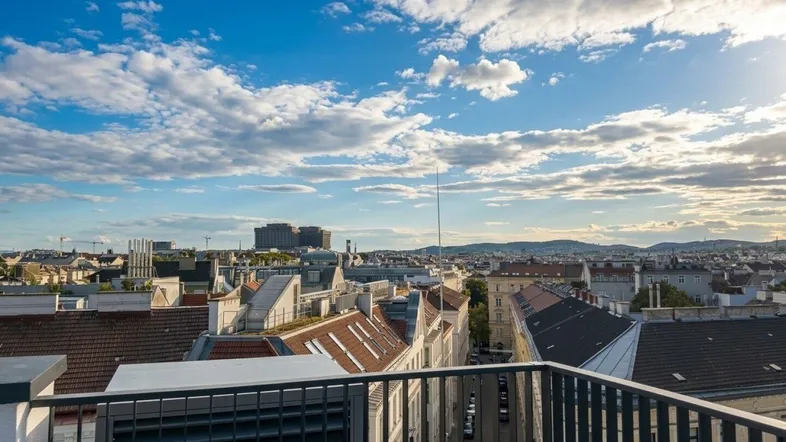 Weitläufiger Blick über die Dächer der Stadt mit blauem Himmel und Wolken.
