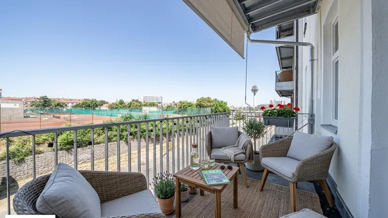 Möblierter Balkon mit Markise, Blick auf Tennisplätze und die Stadt.