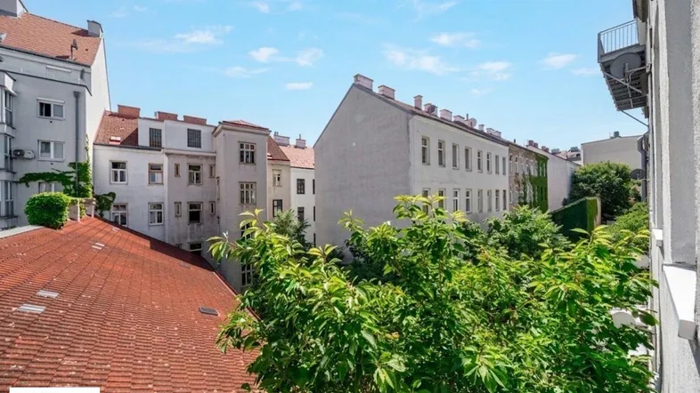 Blick aus dem Fenster auf die umliegenden Gebäude und Dächer mit viel Grün im Vordergrund.
