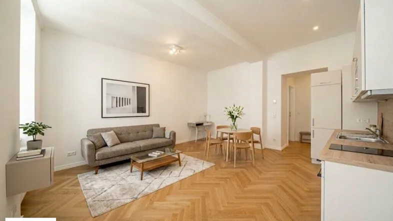 Helles Wohnzimmer mit Fischgrätparkett, integrierter Küchenzeile und modernem Mobiliar.