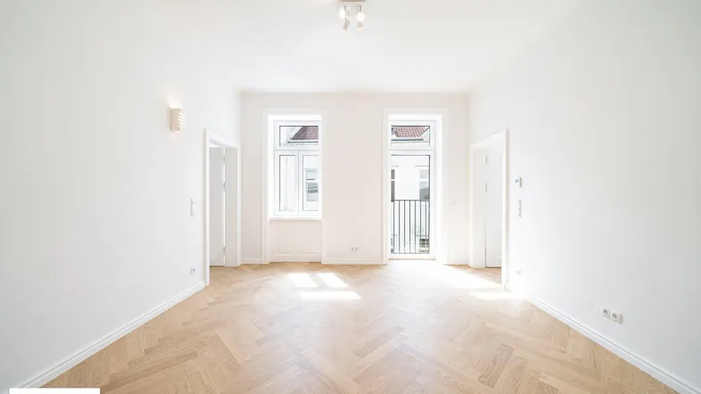 Heller, leerer Raum mit Fischgrätparkettboden und französischen Balkonen, ideal als Wohnzimmer.