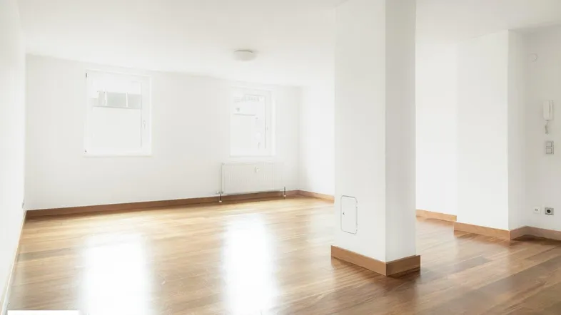 Helles, leeres Zimmer mit Holzboden und weißen Wänden, bereit zur individuellen Gestaltung.
