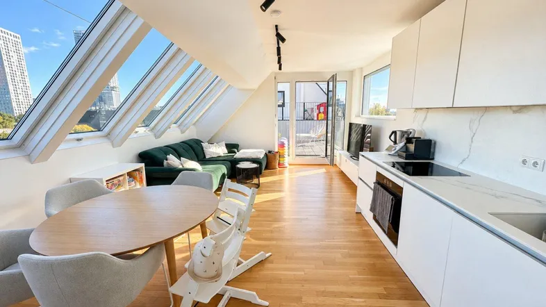 Heller offener Wohn-Essbereich mit integrierter Küche, Parkettboden und Zugang zur Dachterrasse.