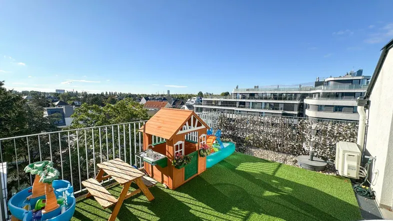 Dachterrasse mit Kunstrasen, Kinderspielhaus und Spielgeräten, ideal für Familien.