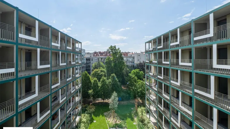 Blick auf moderne Wohngebäude mit begrüntem Innenhof und Balkonen unter blauem Himmel.