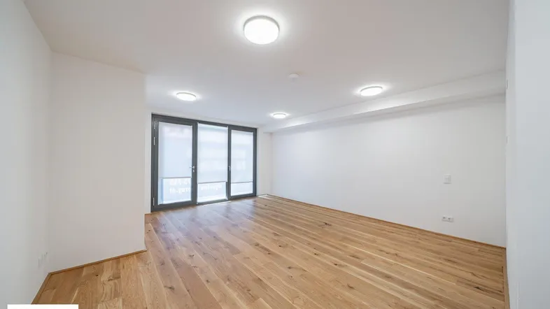 Helles, leeres Zimmer mit Holzboden und großen Fenstern, bereit zur individuellen Gestaltung.