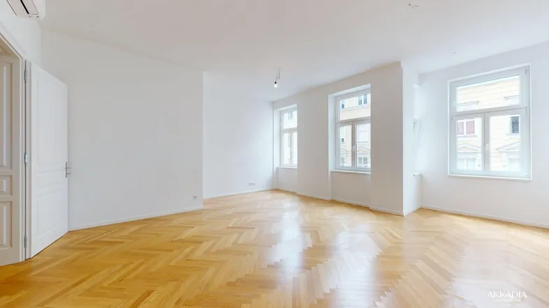 Helles, leeres Zimmer mit Fischgrätparkett und großen Fenstern, bereit zur individuellen Gestaltung.